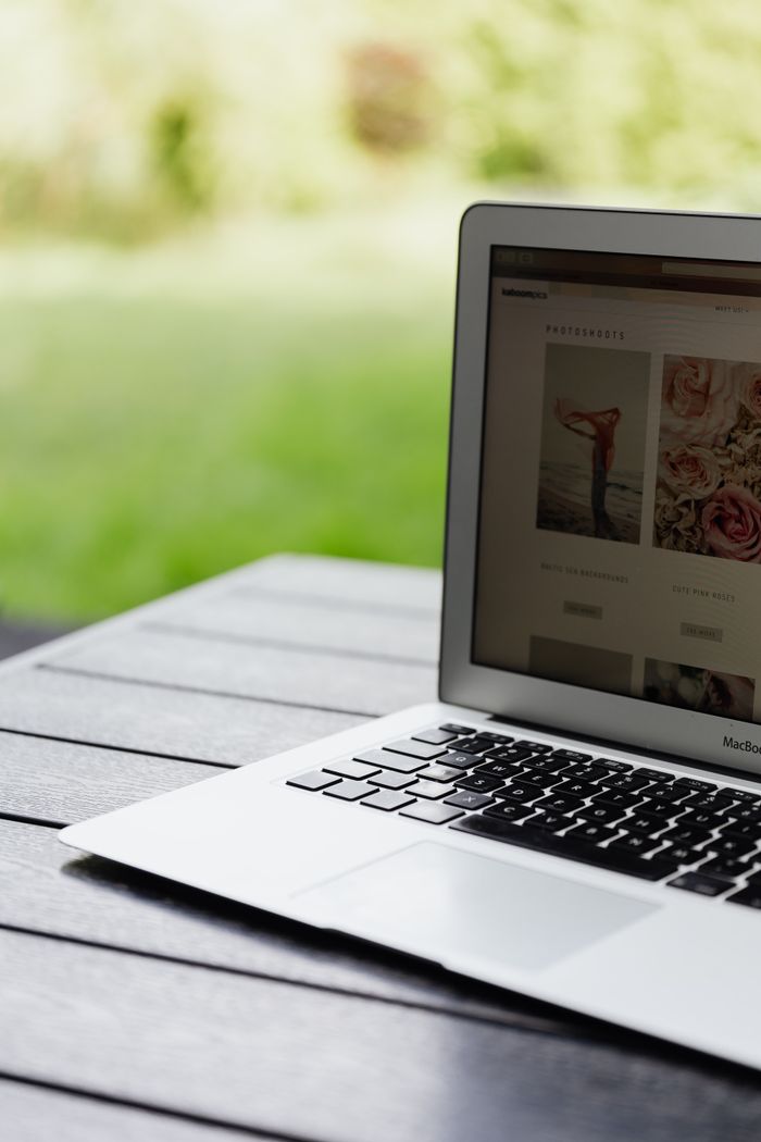 Close-up view of an open laptop resting on a table and showing a website outdoors.